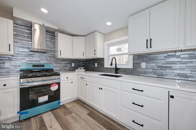 kitchen with stainless steel range with gas cooktop, light wood-style flooring, a sink, light countertops, and wall chimney range hood