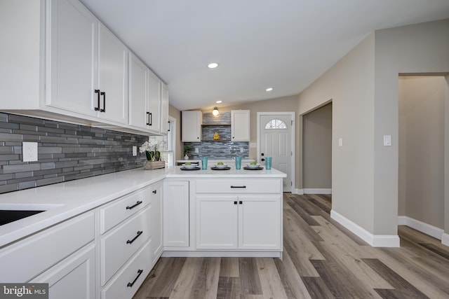 kitchen with a peninsula, vaulted ceiling, white cabinetry, light wood-type flooring, and backsplash