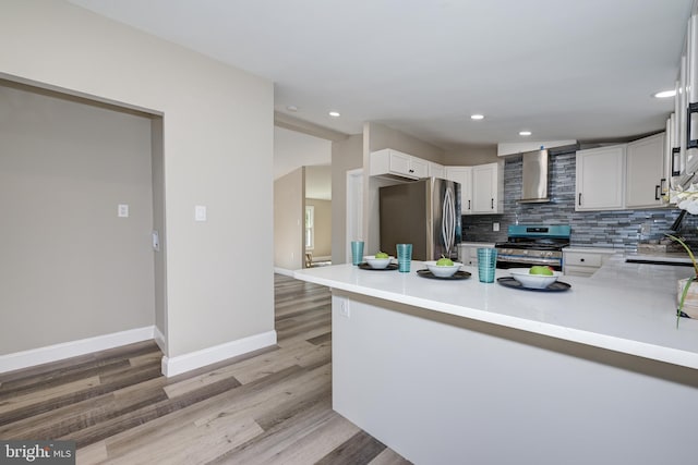 kitchen with light wood finished floors, backsplash, stainless steel appliances, wall chimney exhaust hood, and a sink