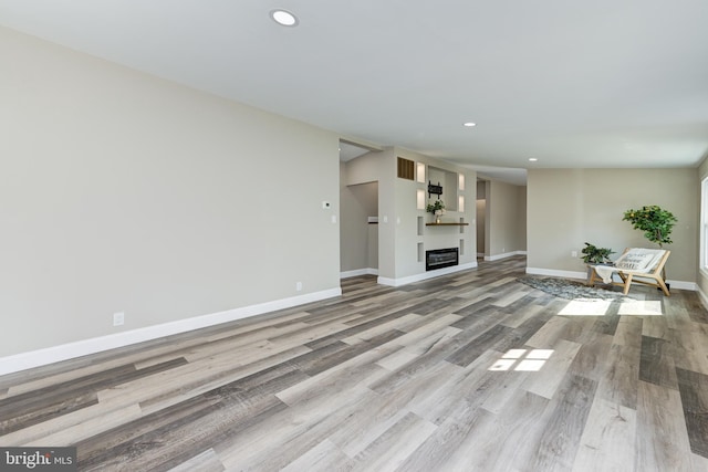 unfurnished living room with a glass covered fireplace, recessed lighting, baseboards, and wood finished floors