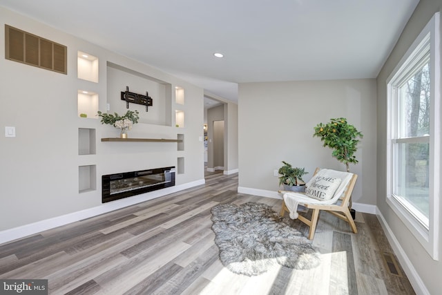 living area featuring a glass covered fireplace, wood finished floors, visible vents, and baseboards