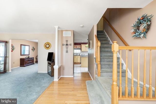 entryway featuring light wood-style flooring, visible vents, baseboards, stairs, and ornate columns