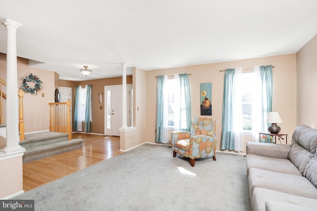 carpeted living area with decorative columns, stairs, baseboards, and wood finished floors