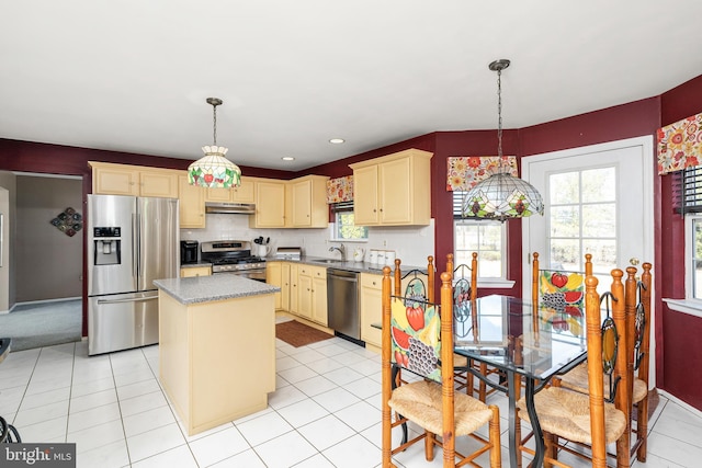 kitchen with under cabinet range hood, a kitchen island, hanging light fixtures, appliances with stainless steel finishes, and cream cabinetry