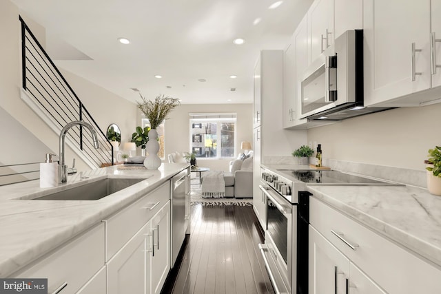 kitchen with dark wood-type flooring, light stone countertops, stainless steel appliances, white cabinetry, and a sink