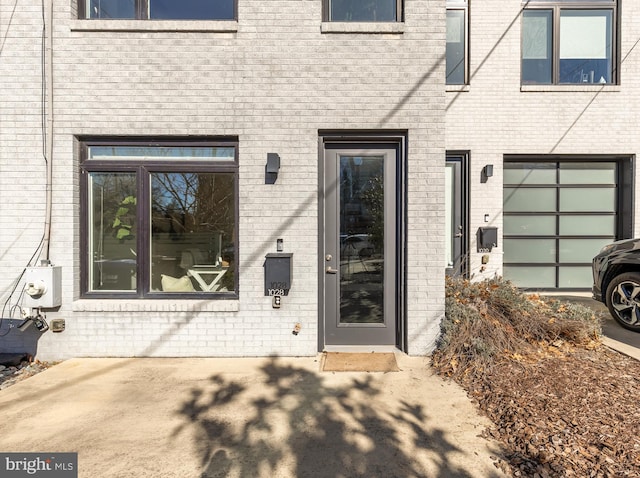 doorway to property with a garage, a patio, and brick siding