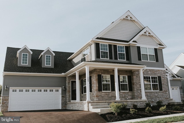 craftsman-style house featuring a porch, a garage, driveway, stone siding, and roof with shingles