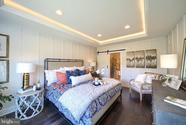 bedroom featuring a raised ceiling, a decorative wall, dark wood-style flooring, and a barn door