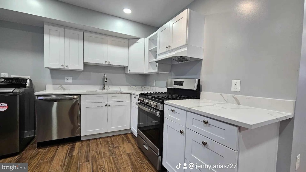 kitchen featuring appliances with stainless steel finishes, washer / clothes dryer, dark wood-type flooring, white cabinetry, and a sink