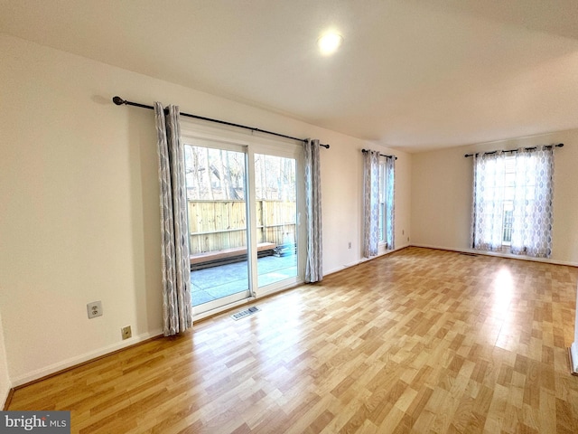 spare room featuring a wealth of natural light, visible vents, light wood-style flooring, and baseboards