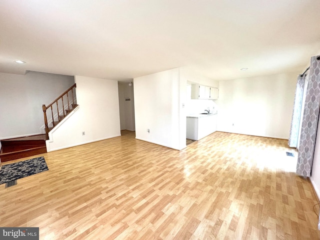 unfurnished living room featuring baseboards, visible vents, stairs, light wood-style floors, and a sink