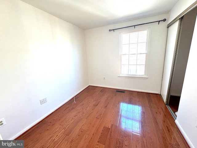 unfurnished bedroom with a closet, visible vents, baseboards, and wood finished floors