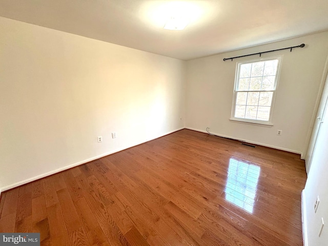 spare room with visible vents, baseboards, and wood finished floors