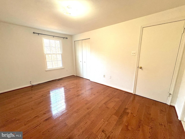 unfurnished bedroom with a closet, visible vents, baseboards, and wood finished floors