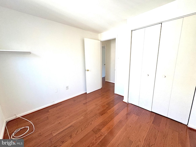 unfurnished bedroom with dark wood-style flooring, a closet, and baseboards