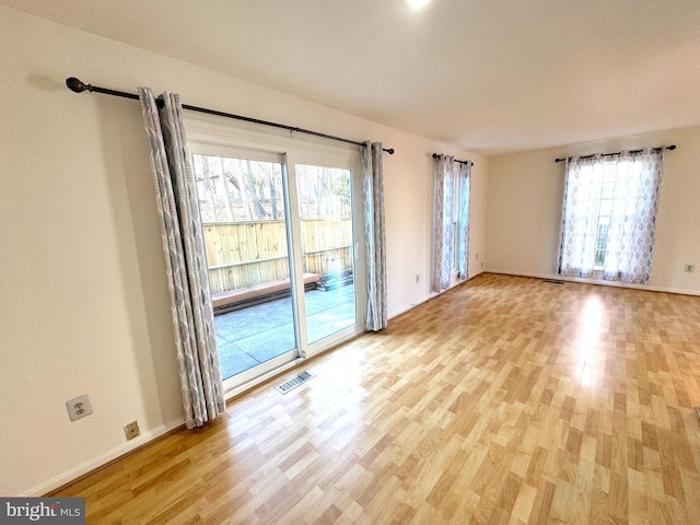 spare room featuring light wood-type flooring, visible vents, and baseboards