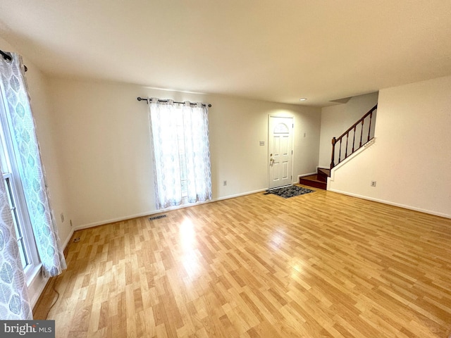 unfurnished living room featuring stairway, light wood-style flooring, visible vents, and baseboards