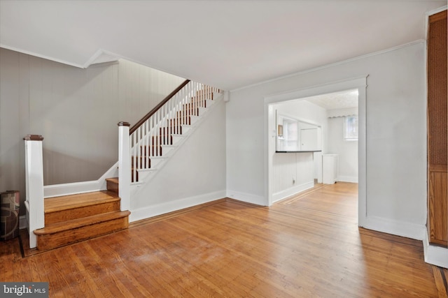 unfurnished living room with crown molding, stairs, baseboards, and wood finished floors