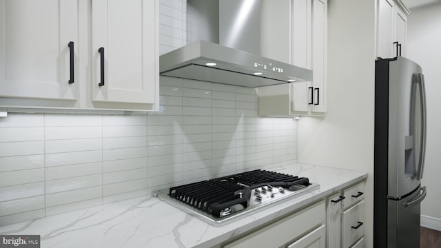 kitchen featuring white cabinets, decorative backsplash, appliances with stainless steel finishes, light stone countertops, and wall chimney range hood