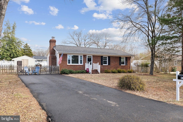 single story home featuring brick siding, a fenced front yard, a chimney, and aphalt driveway