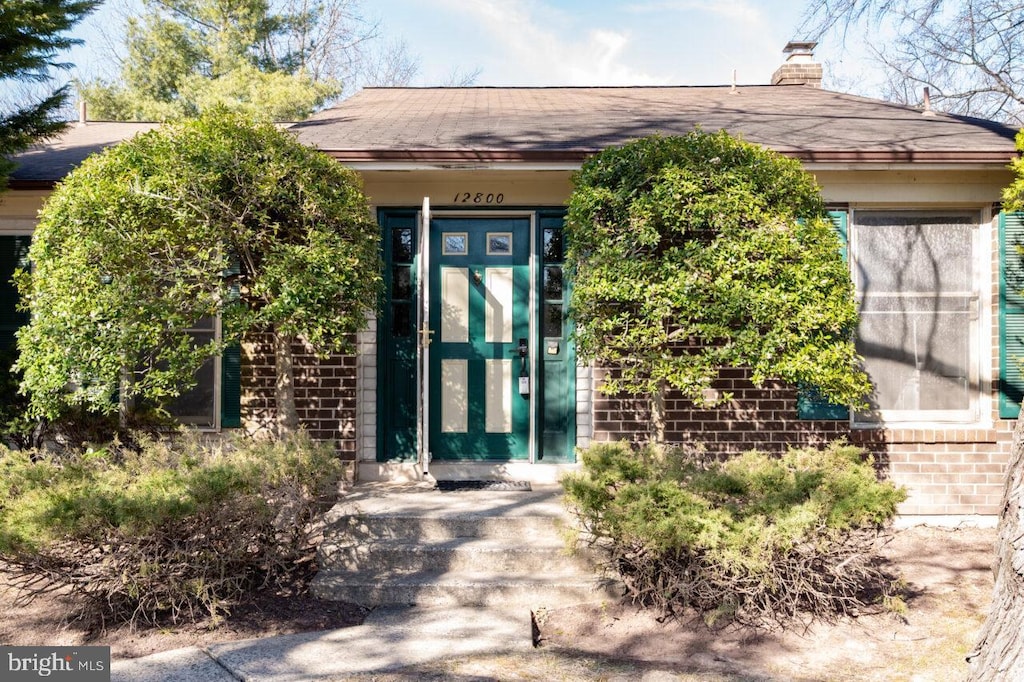 view of exterior entry with brick siding and a chimney