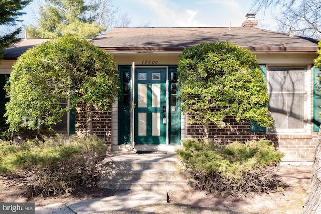 doorway to property with brick siding and a chimney