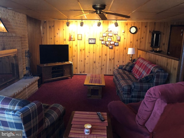 carpeted living room with a ceiling fan, a fireplace, and wood walls