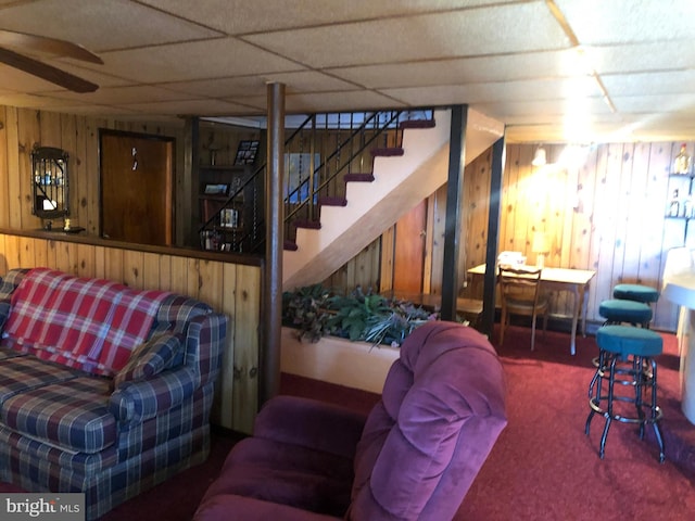 living room with wooden walls, stairway, a drop ceiling, and carpet flooring