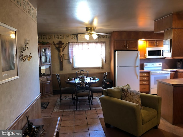 kitchen featuring a wainscoted wall, white appliances, light tile patterned floors, and a ceiling fan