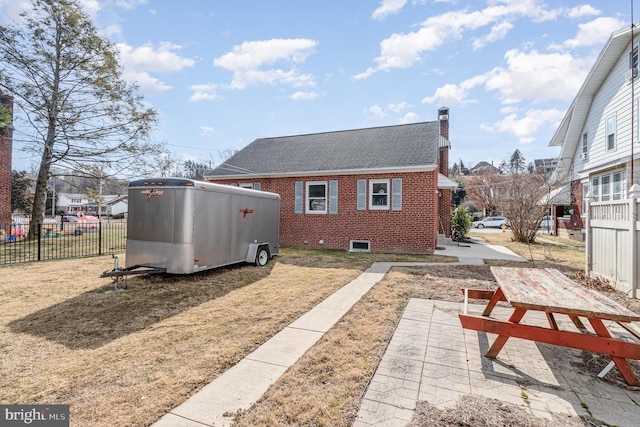 view of home's exterior featuring brick siding, a yard, a chimney, roof with shingles, and fence