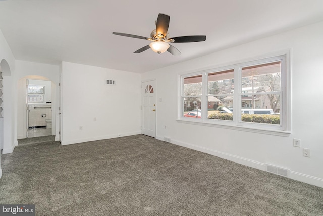 unfurnished living room with visible vents, arched walkways, dark colored carpet, and baseboards