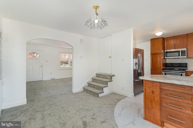 kitchen featuring arched walkways, brown cabinets, stainless steel appliances, light countertops, and decorative backsplash