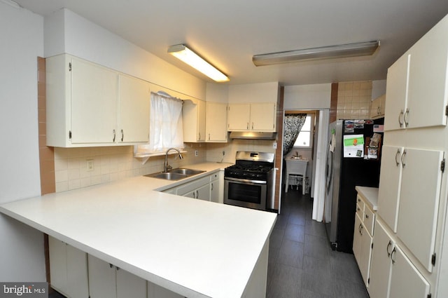 kitchen featuring tasteful backsplash, appliances with stainless steel finishes, a sink, a peninsula, and under cabinet range hood