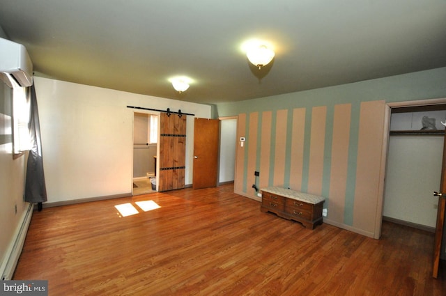 unfurnished bedroom featuring a baseboard radiator, a barn door, an AC wall unit, wood finished floors, and baseboards