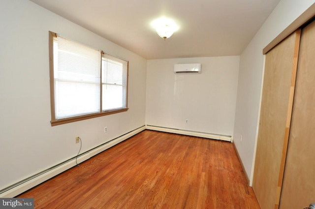 unfurnished room with an AC wall unit, baseboard heating, and wood finished floors