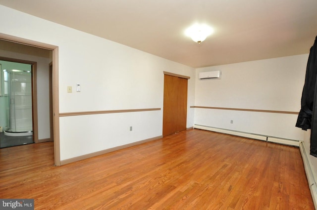 empty room with a baseboard heating unit, an AC wall unit, light wood-type flooring, and baseboards