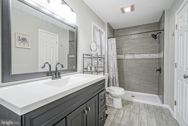 bathroom with visible vents, vanity, toilet, and tiled shower