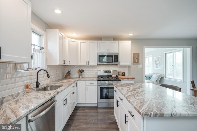 kitchen with stainless steel appliances, dark wood-type flooring, a sink, white cabinets, and light stone countertops