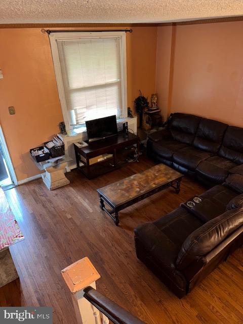 living area with a textured ceiling, ornamental molding, and wood finished floors