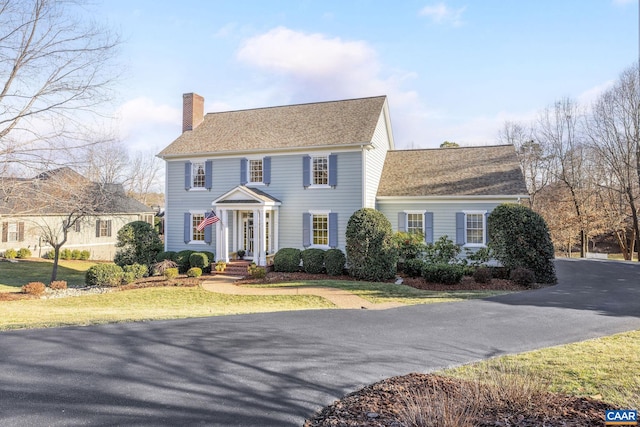 view of front of house featuring a shingled roof, a chimney, and a front lawn