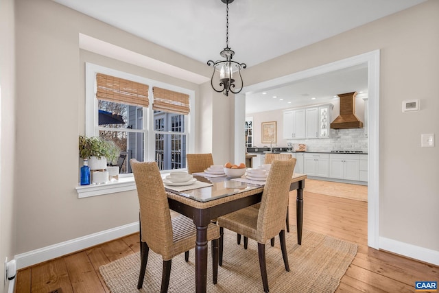 dining space with light wood-type flooring, baseboards, and a notable chandelier