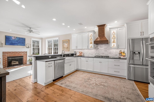 kitchen featuring dark countertops, appliances with stainless steel finishes, light wood-style floors, premium range hood, and a peninsula