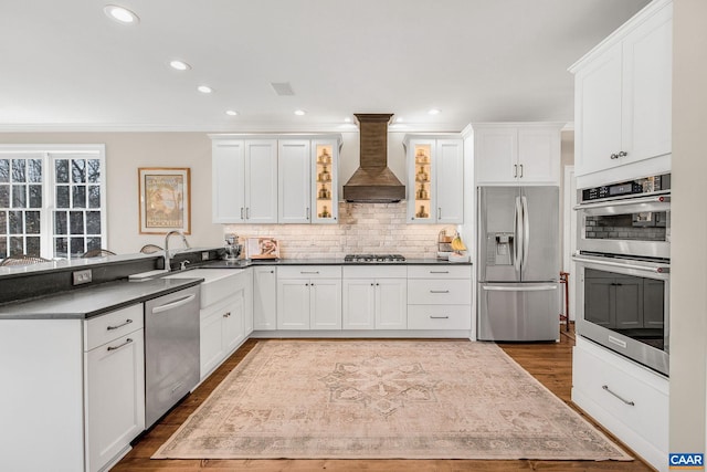 kitchen with a peninsula, white cabinets, appliances with stainless steel finishes, decorative backsplash, and custom range hood