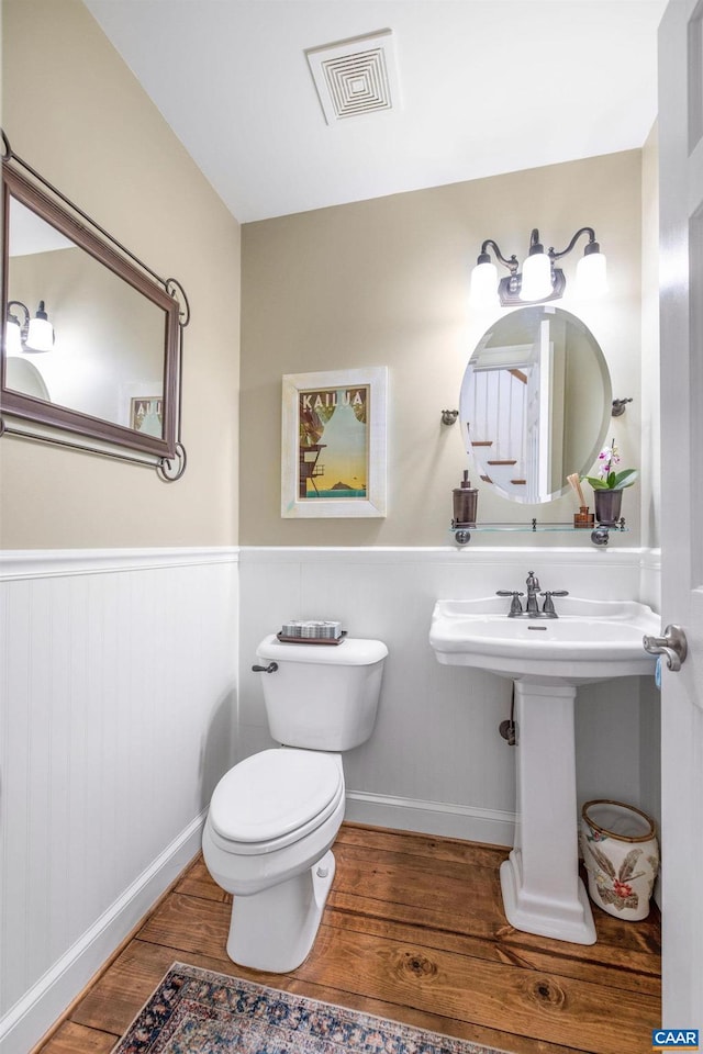 half bathroom with toilet, a wainscoted wall, visible vents, and wood finished floors