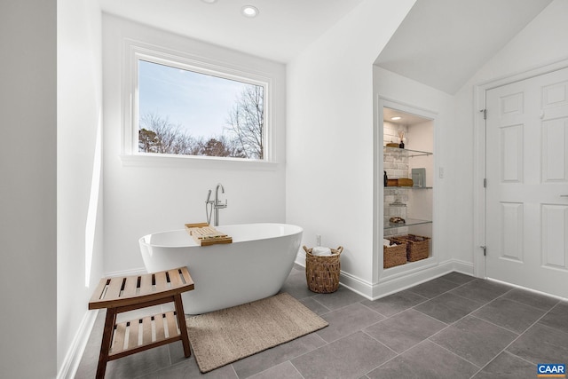 bathroom featuring lofted ceiling, baseboards, a tile shower, and a freestanding bath