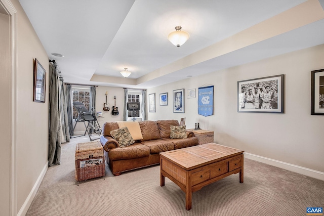 living room with a raised ceiling, light carpet, and baseboards