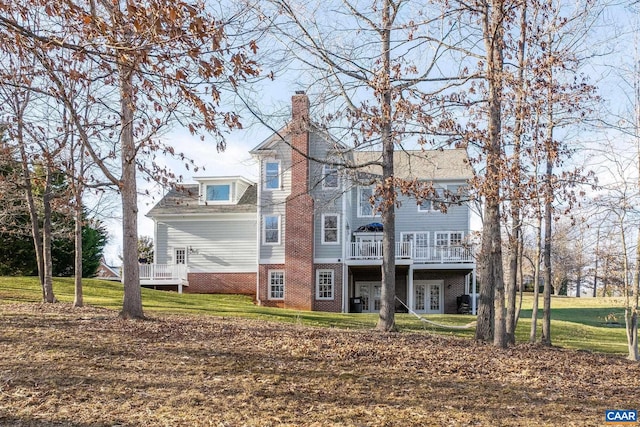 rear view of house with brick siding, a yard, french doors, a wooden deck, and a chimney