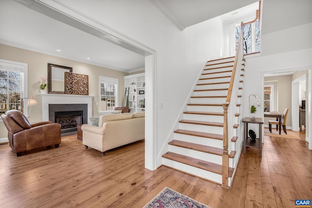 stairway featuring ornamental molding, wood-type flooring, a fireplace, and baseboards