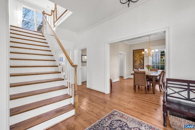 foyer with stairway, light wood-type flooring, an inviting chandelier, and crown molding