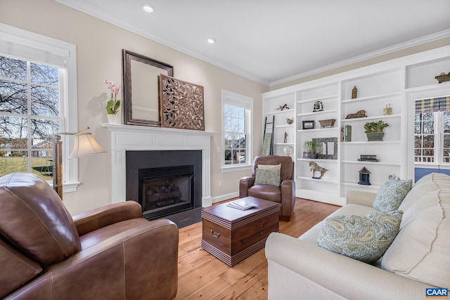 living area with light wood-style floors, recessed lighting, ornamental molding, and a fireplace with flush hearth